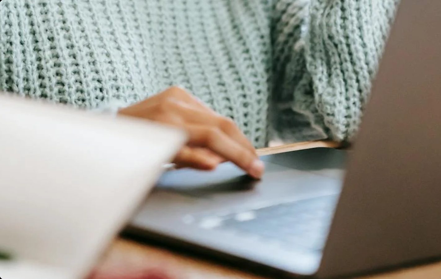 A woman in a mint knit sweater working at a laptop