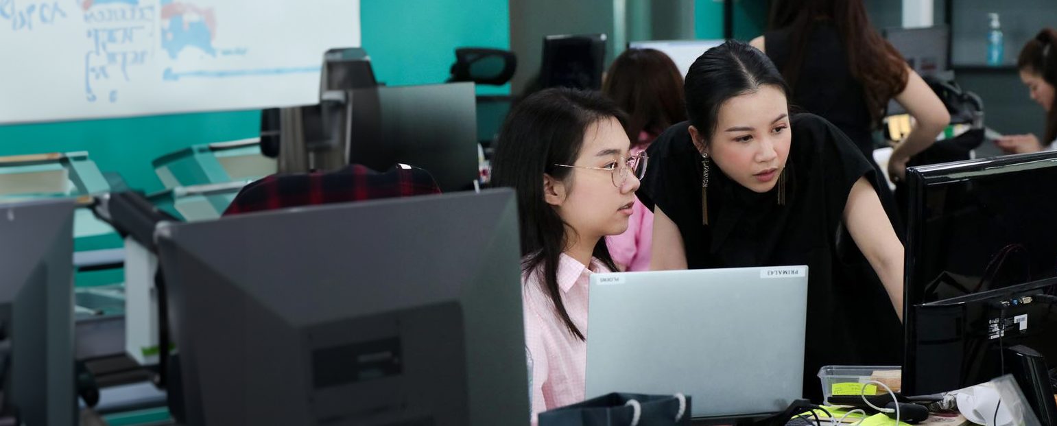 Two women working at a desktop computer and a laptop in Primal's office