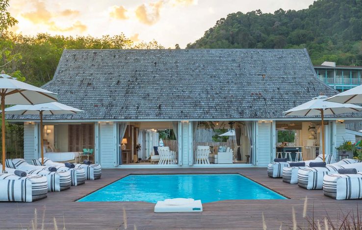 A resort pool lined with sun loungers beside a tiled pavilion
