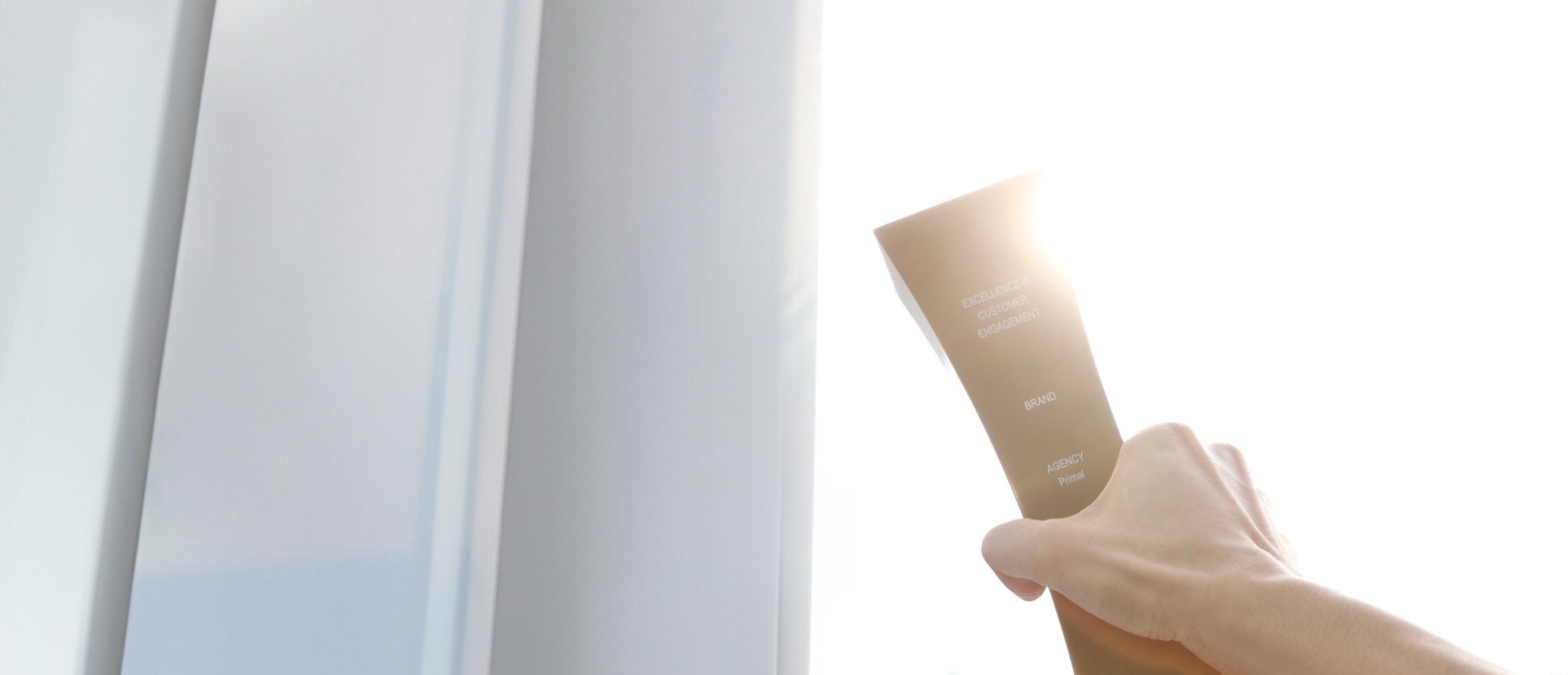 A hand holding a product tube engraved with the words EXCELLENCE, BRAND and AGENCY