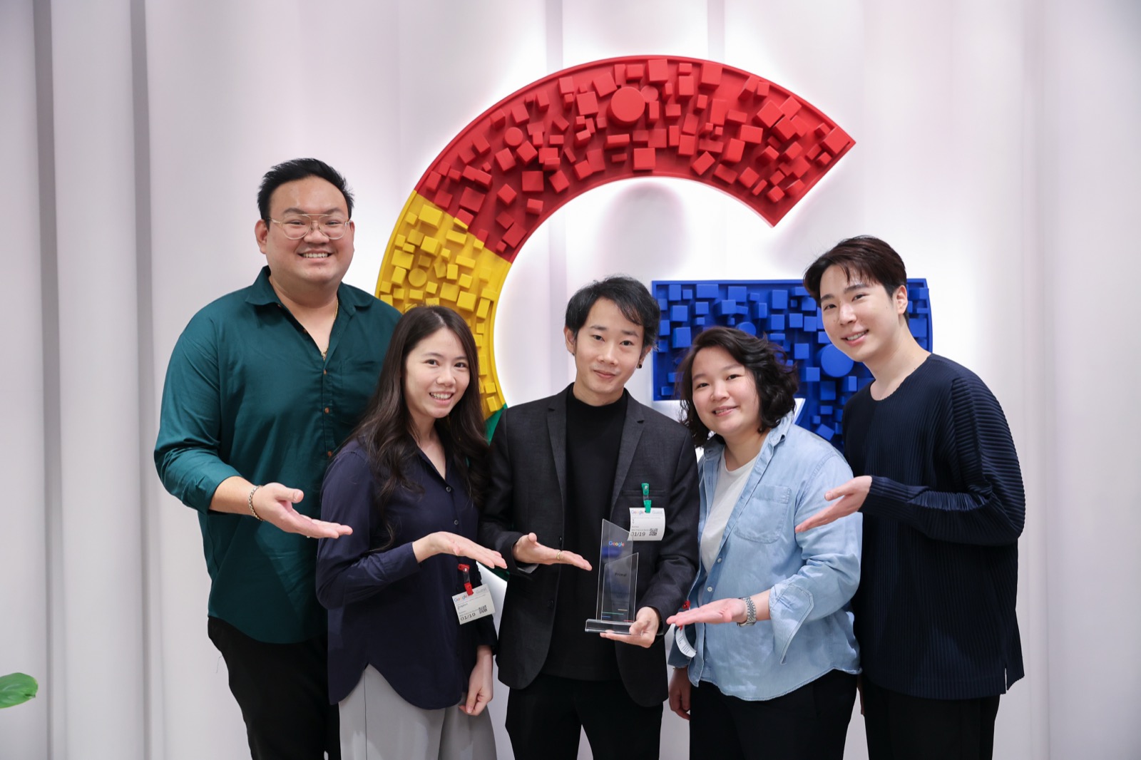 Five Primal team members holding trophies in front of a curved red, yellow and blue logo wall