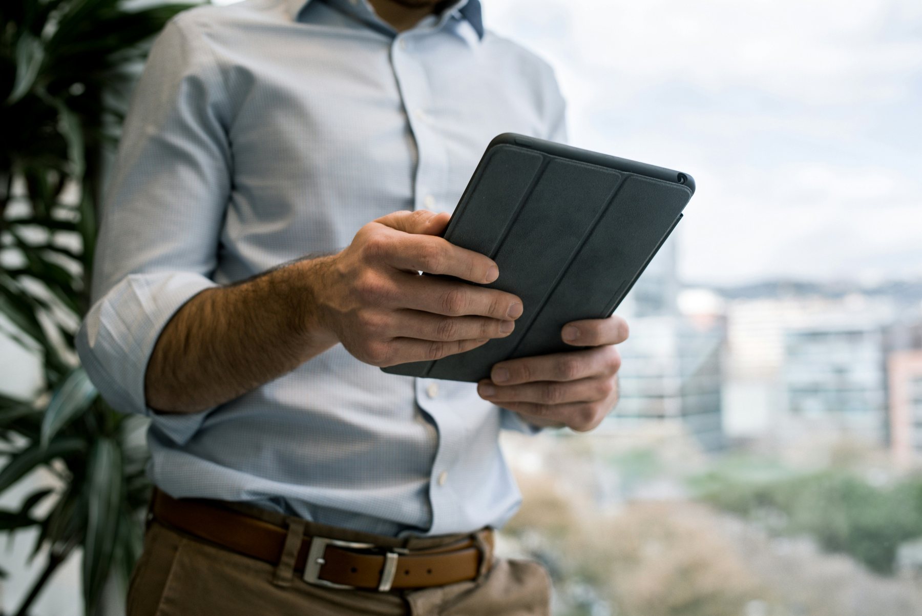 A person in a light blue shirt holding a tablet beside an office window