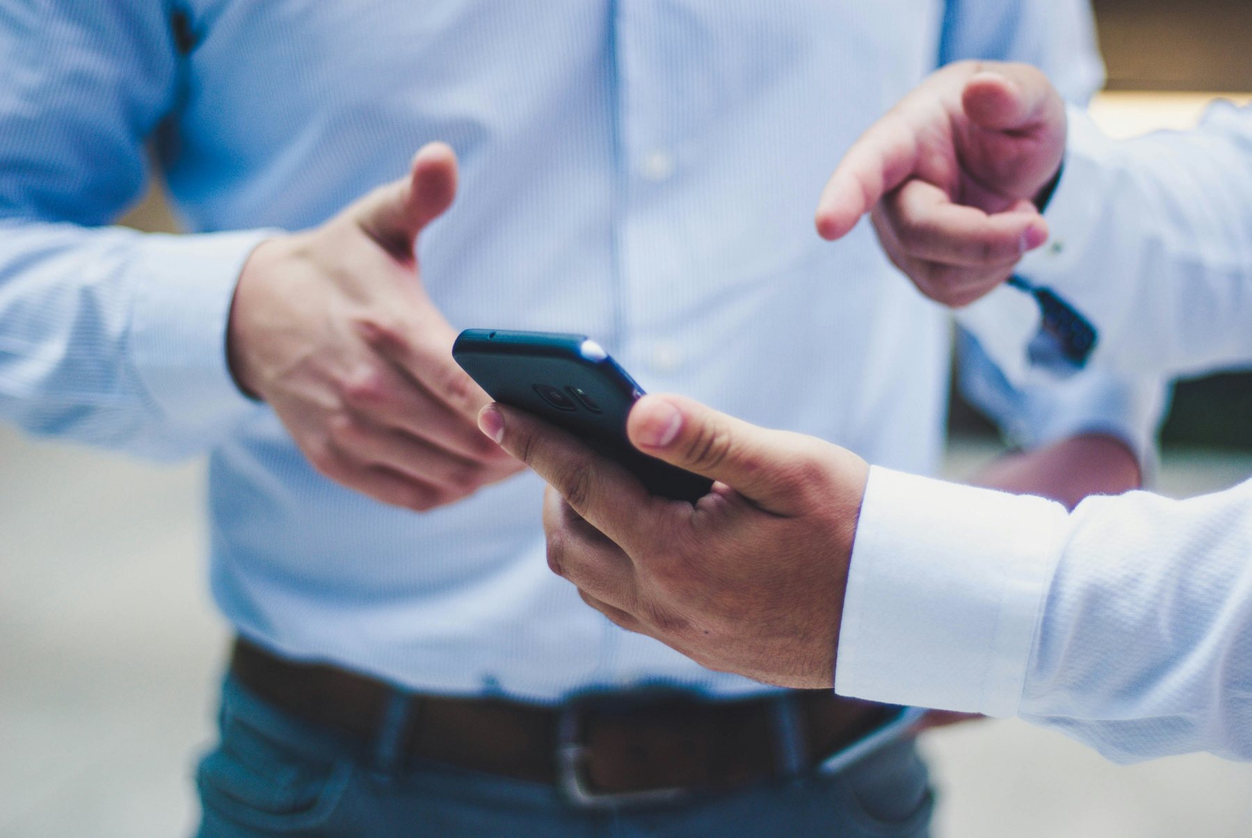 Two people in business shirts exchanging a smartphone during a meeting