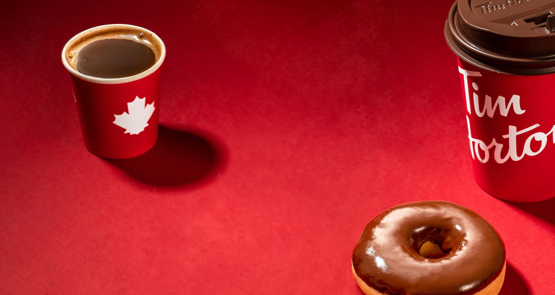 A red Tim Hortons coffee cup and a chocolate-glazed doughnut on a red background