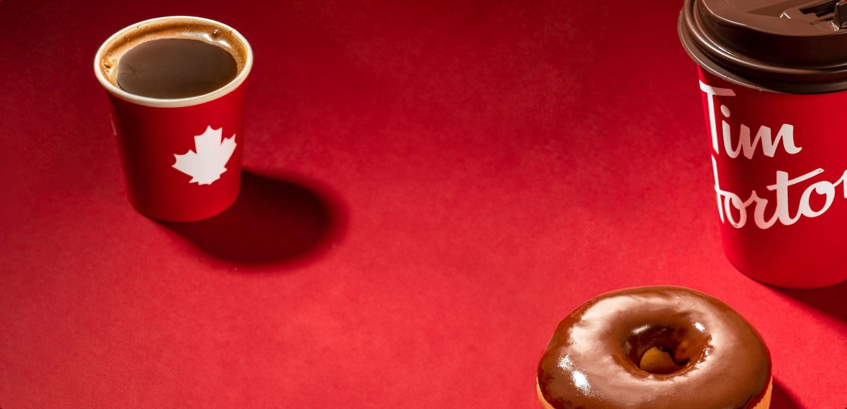 A Tim Hortons red cup and a chocolate-dipped doughnut on red